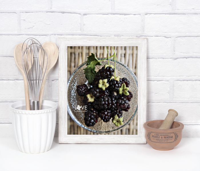 White kitchen setting with a framed color photo of handpicked fresh, plump blackberries in a clear bowl