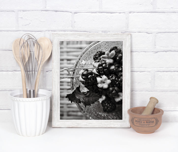 white kitchen setting with a framed black and white photo of handpicked fresh, plump blackberries in a clear bowl